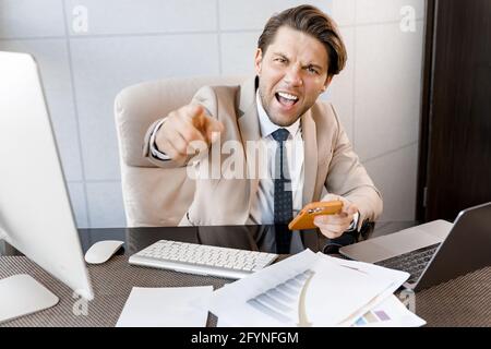 Happy young businessman in costume looking at camera,give motivation, happy successful winner man sitting at office desk showing finger for business Stock Photo