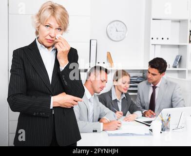 Business team tensely solving problems in office with upset woman foreground Stock Photo
