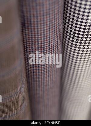 Closeup stack of warm wooled tweed textile rolls with different patterns. Sale or tailoring objects concept. Fabrics retail store, atelier, drapery or textile shop. High quality vertical photo Stock Photo