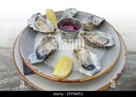 plate with fresh opened oysters and dip on a wooden table, gradient isolated in white back Stock Photo