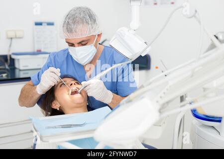 Man dentist holding dental drill and treating teeth of girl in dentist office Stock Photo