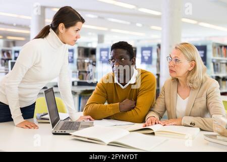Female tutor helping students preparing for exam in library Stock Photo