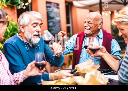 Happy retired friends having fun drinking red wine at pre dinner party - Senior people eating at restaurant together - Dinning life style concept Stock Photo
