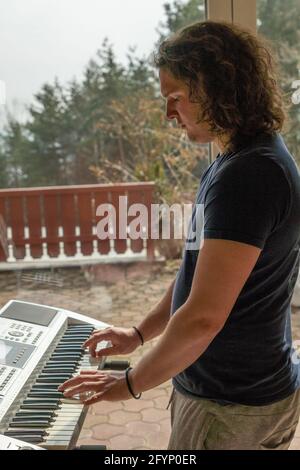Vertical shot of a middle eastern male with curly long hair playing the synthesizer Stock Photo