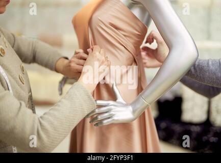 Fashion, dressmaking or tailoring concept. Professional team of tailors, dressmakers or designers working with new model applying linen fabrics beige cloth on mannequin or dummy in atelier Stock Photo