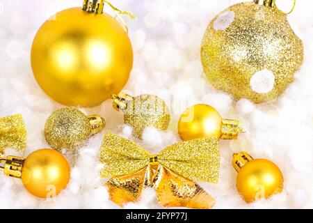 Bright golden Xmas decorations (ribbons, baubles, bows, ornament) on white artificial snow background with copy space. Christmas and New Year traditio Stock Photo