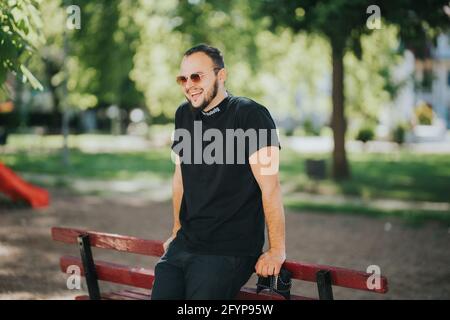 Carefree young male leaning on a park bench is spending leisure time in the park Stock Photo