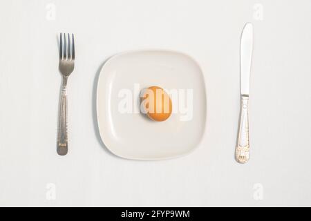 Raw egg, fork and knife on a blue plate on a white napkin Stock Photo