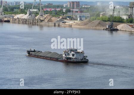 The tug transports a barge loaded with sand along the river. Stock Photo