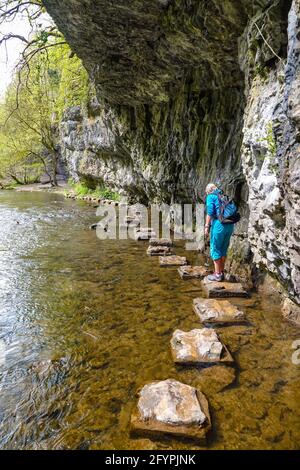 Single female hiker on Stepping stones, that form a path along the side of the River Wye, Cheedale, near Buxton, Peak District, Derbyshire Stock Photo