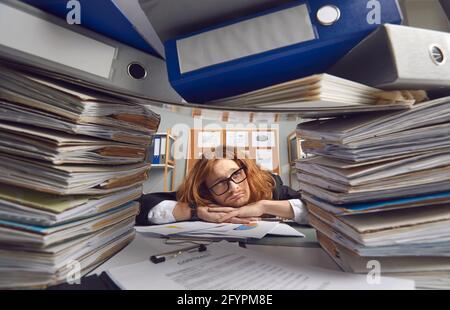 Tired office worker sitting at desk and looking apathetically at piles of paperwork Stock Photo
