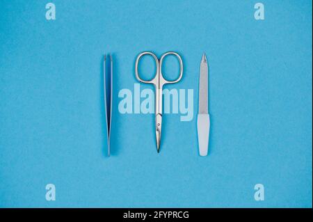 blue background, in the center are lying tweezers, nail file and nail scissors Stock Photo