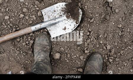 Black boots with a shovel on black earth. Farmer with a shovel. A man in vintage boots on black ground. Stock Photo