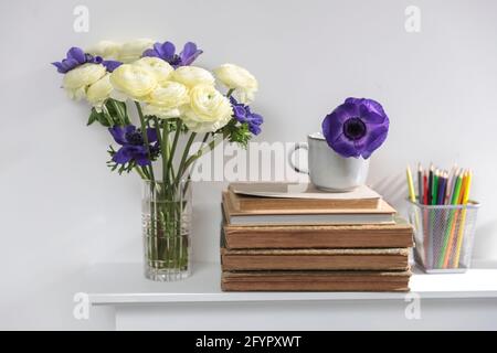 One blue anemone in a cup in the style of the seventies on the table with pile ofbooks as an interior decoration. Pencil holders with pencils and a va Stock Photo