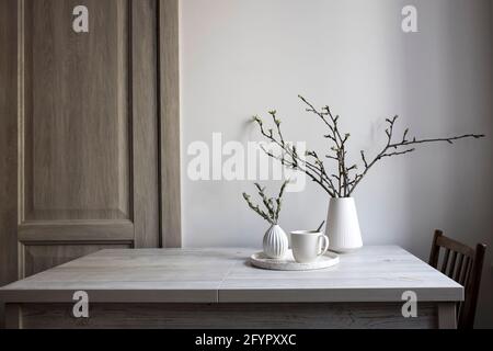Minimalistic Scandinavian style. Half-open branches of an apple tree in a white fluted vase. A small vase with a branch of dried eucalyptus and a cup Stock Photo