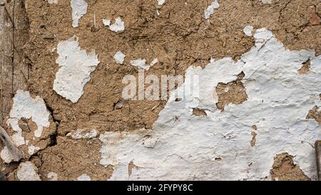 Peeling white paint on an ancient wall of clay and straw. The wall of an ancient hut. Stock Photo