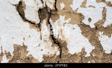 The texture of the split wall is ancient. A wall of clay and straw. The hut is old. Peeling paint on a vintage wall with cracks Stock Photo