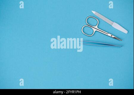 nail scissors, tweezers and nail file lying on blue background with copy space Stock Photo