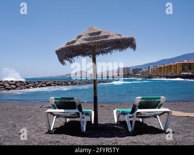 View from the lava beach over the Atlantic Ocean and the place 'Punta Larga' on the south coast of the island of Tenerife. In the foreground two empty Stock Photo