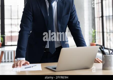 Businessman in suit standing at work desk with laptop and document Stock Photo