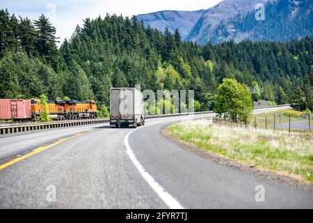 Classic big rig industrial semi truck with semi trailer for for transporting animals running on curving highway road with green mountain forest in Col Stock Photo
