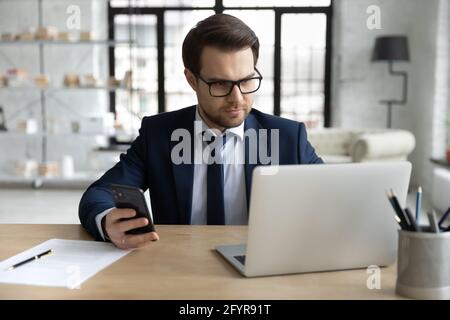 Focused business professional using laptop and mobile phone for work Stock Photo