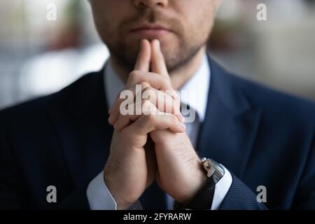Clasped hands of business leader touching chin in deep thoughts Stock Photo