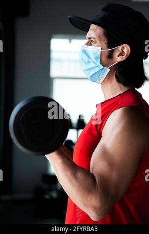 Fit mexican guy training curl biceps at gym during COVID pandemic Stock Photo