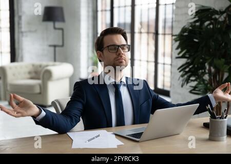 Peaceful business leader meditating at workplace, making zen hands Stock Photo