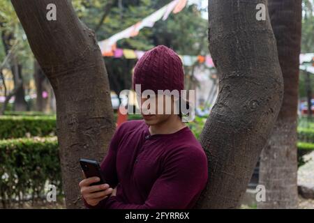 Young hispanic man with beanie looking at his cellphone Stock Photo