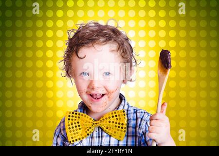 Lovely young child holding chocolate covered cooking spoon when mixing icing for an easter cake, on yellow polka-dot background