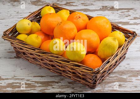A closeup of lemons and oranges in a wicker basket, on a wooden surface Stock Photo