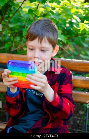 8-years old boy playing with popit in park. happy child with toy. kid wearing bright summer casual clothes. multicolored pop it close-up. Stock Photo