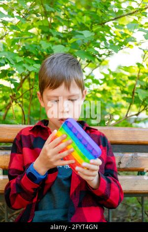 8-years old boy playing with popit in park. happy child with toy. kid wearing bright summer casual clothes. multicolored pop it close-up. Stock Photo