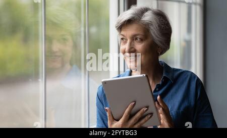 Attractive middle-aged woman holding tablet looking out the window Stock Photo