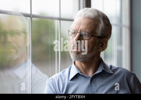 Mature thoughtful man standing indoor looking out the window Stock Photo