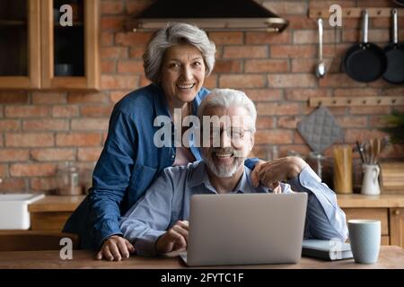 Mature spouses family spend time together in kitchen with laptop Stock Photo
