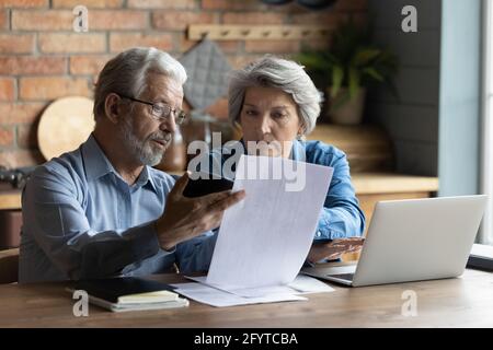 Focused worried older spouses reading financial documents checking bills Stock Photo