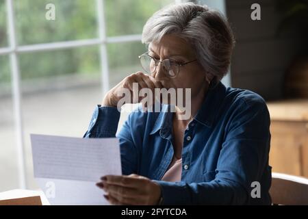 Middle aged female reading letter looking concerned Stock Photo