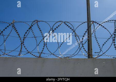 concrete wall and tangled iron barbed wire on blue sky background Stock Photo