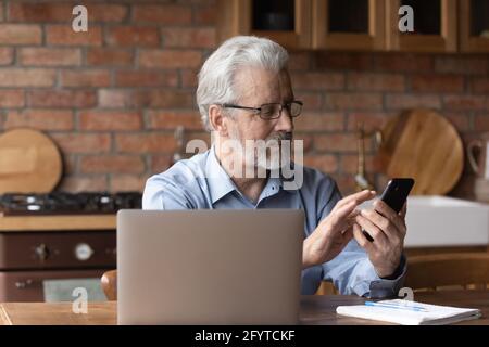 Bearded mature man sit in kitchen with smart phone Stock Photo