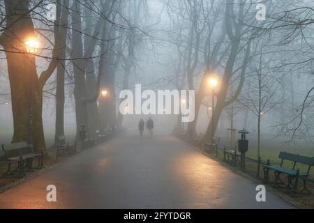KRAKOW, POLAND - DECEMBER 06, 2015: Couple walking in mist. October morning in Planty Park, Krakow, Poland. Stock Photo