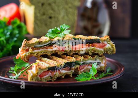 Vegetarian sandwich panini with spinach leaves, tomatoes and cheese on a dark table. Toast with cheese. Stock Photo