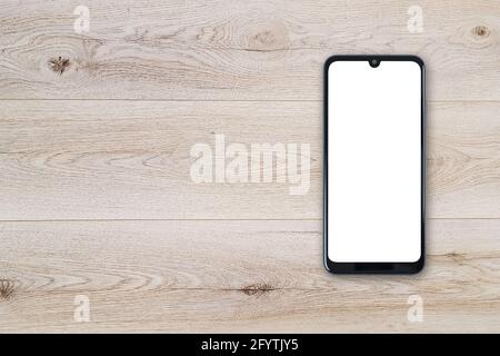 Top view of a new modern black frameless smartphone mockup with blank white screen on a wooden table (copy space). Stock Photo