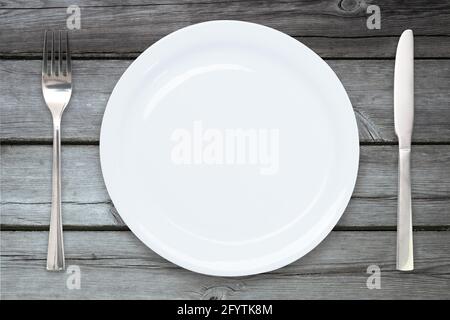 Cooking template - top view of an empty ceramic white plate with cutlery on a wooden vintage table Stock Photo