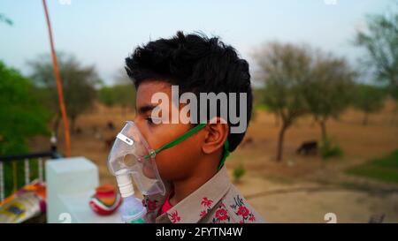 A Little boy breathing with oxygen mask at home. Indian Child Patient infected with Covid 19 disease. Indian boy taking treatment of Asthma, lungs. Stock Photo