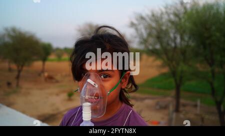 A Little Baby breathing with oxygen mask at home. Indian Girl Patient infected with Covid 19 disease.Female taking treatment of Asthma, lungs. Stock Photo
