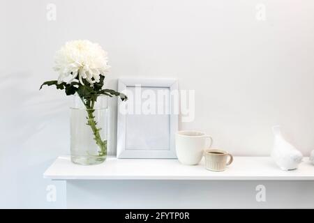 Large chrysanthemum in a glass vase. Photo frame with place for text, two corrugated cups with coffee and ceramic figurines of birds on the table. Off Stock Photo