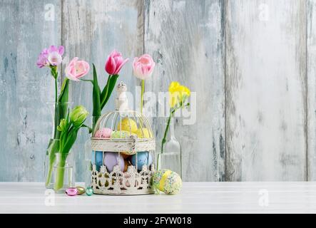 Basket with Easter eggs and flowers in glass bottles. Spring home decoration. Stock Photo