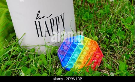 New popular silicone colorful antistress pop it toy for child on the grass near the box with the inscription Be happy. Copy space. Simple dimple Stock Photo